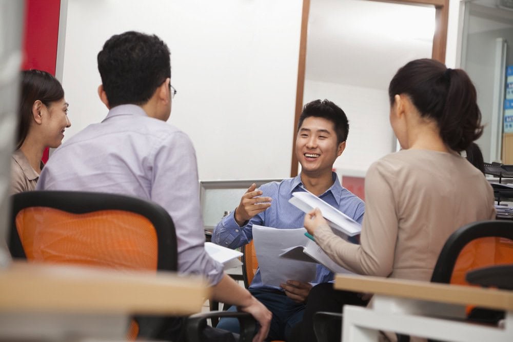 Four smiling Asian professionals engaged in a discussion, representing a productive meeting between a customer and an IT vendor to determine the best IT support solution.